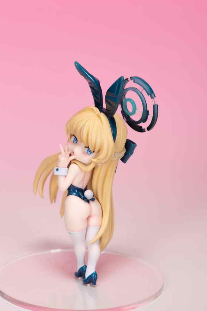 A collectible figure of a character in a bunny girl costume with long blonde hair, wearing thigh-high stockings and high heels, set against a pink background.