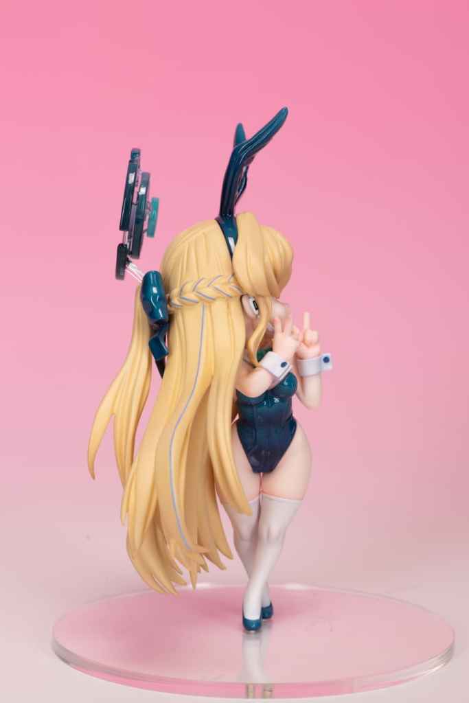 バニーガール衣装を着たキャラクターの後ろ姿を示すフィギュア。キャラクターは長い金髪で、頭にはウサギの耳が付いている。背景はピンク色。