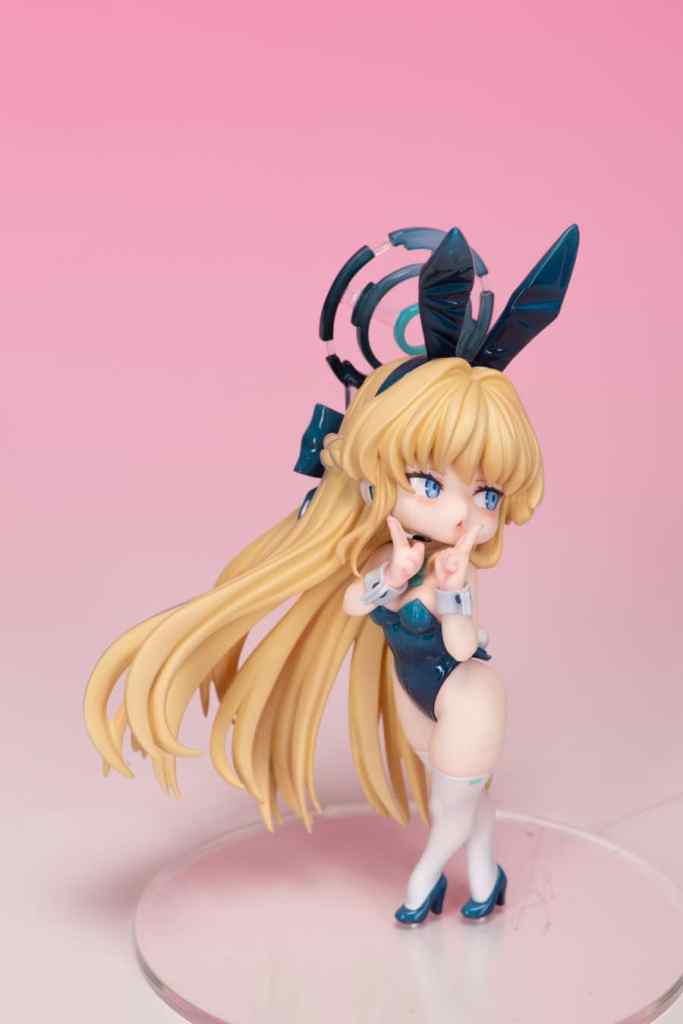 A detailed figure of a character styled as a bunny girl with long blonde hair, wearing a blue outfit and white stockings, posed playfully against a pink background.