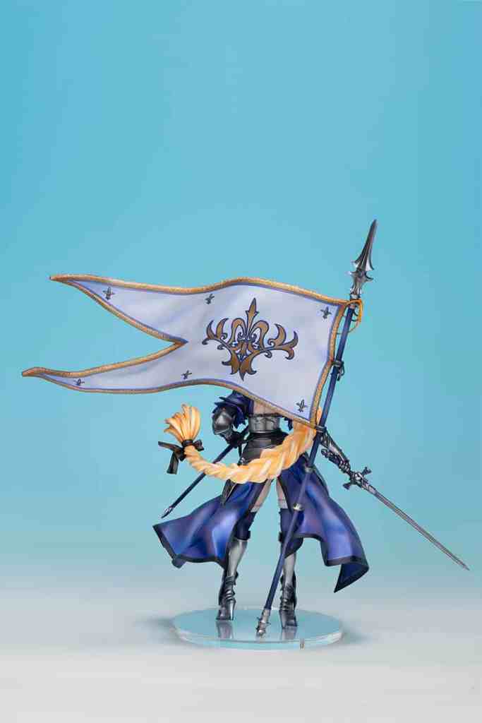 Fate/Grand Orderのジャンヌ・ダルクのフィギュア、青い背景に立っており、旗を持っている。