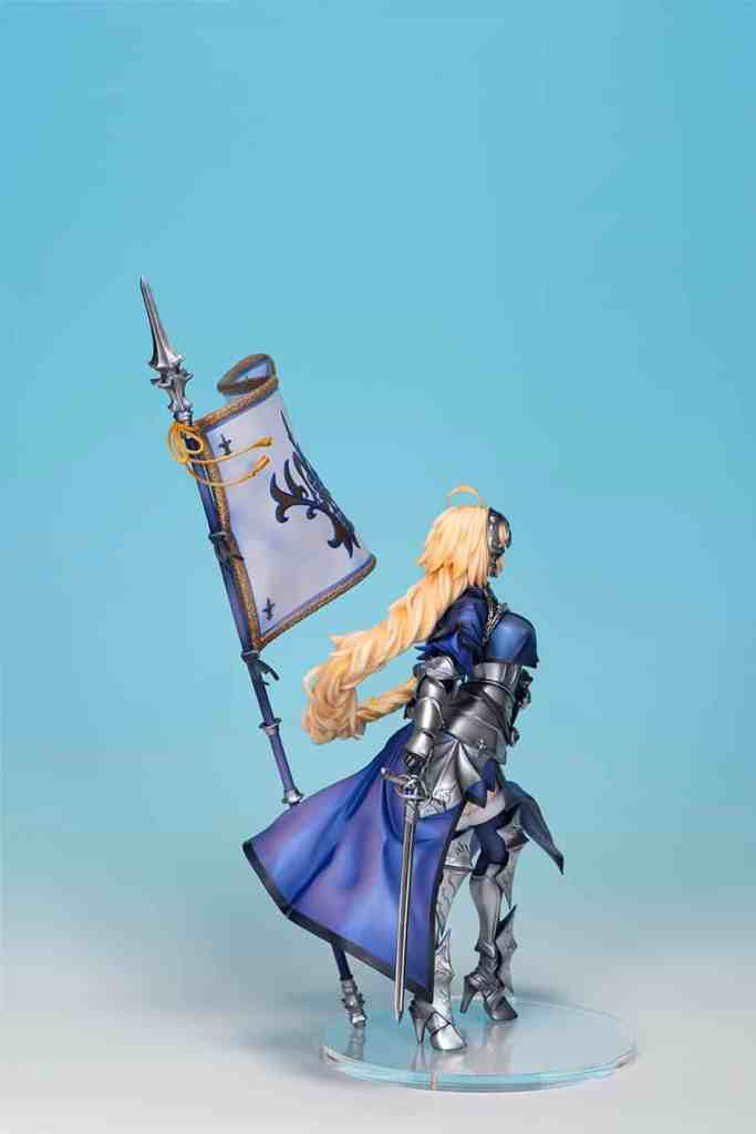 A detailed figure of Jeanne d'Arc from Fate/Grand Order, featuring her in a blue outfit with armor, holding a flag and sword, posed against a light blue background.