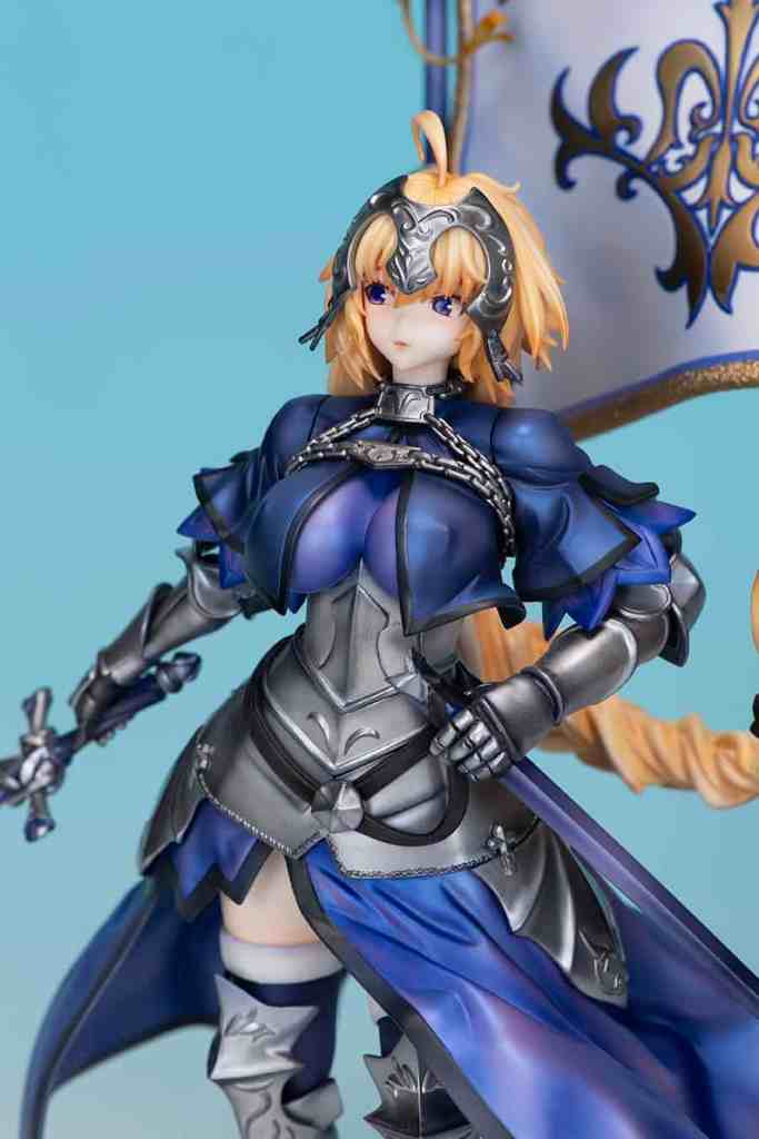 フィギュアのジャンヌダルクは、青と銀の甲冑を身に着け、剣を持って立っている姿を捉えたものです。背景は淡い青色で、彼女の衣装の詳細が際立っています。