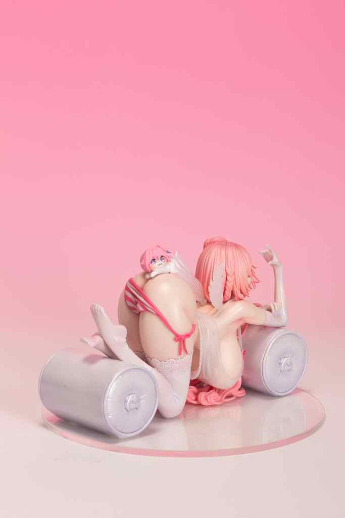 A figurine featuring a character with pink hair and a playful pose, set against a soft pink background. The figure showcases detailed craftsmanship and vibrant colors.