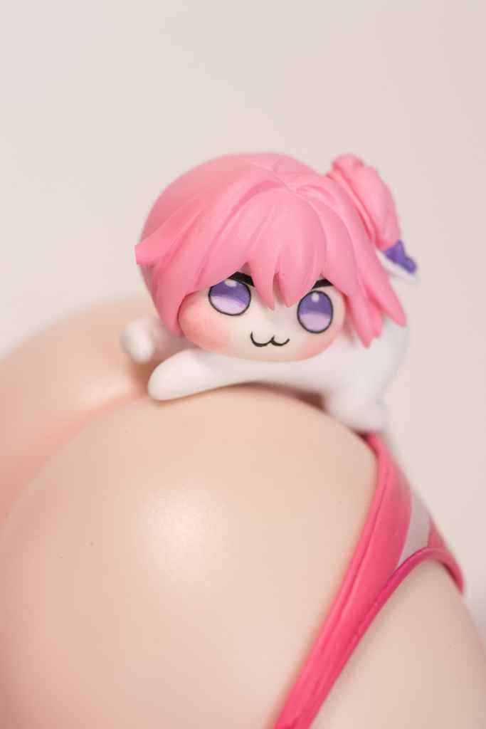 Close-up of a collectible figure with pink hair and a playful expression, resting on a semi-bare rounded surface, dressed in a pink swimsuit.