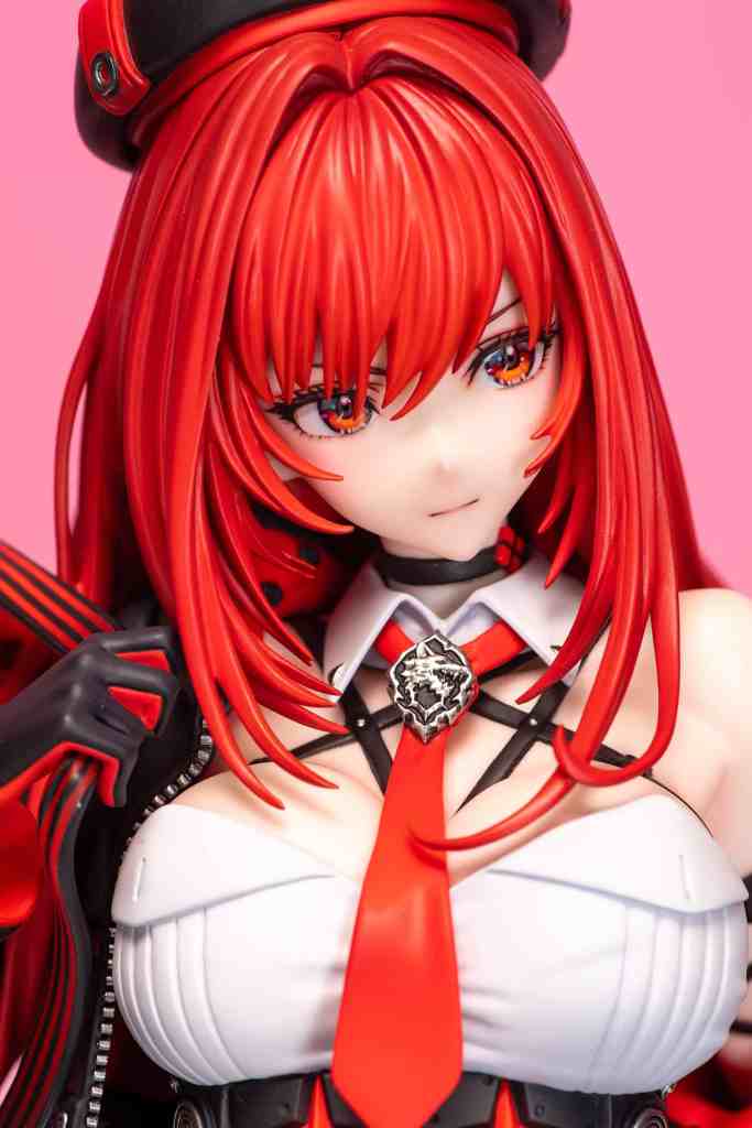 Close-up of a red-haired figurine wearing a black hat, a white top with a red tie, and a black arm guard, set against a pink background.
