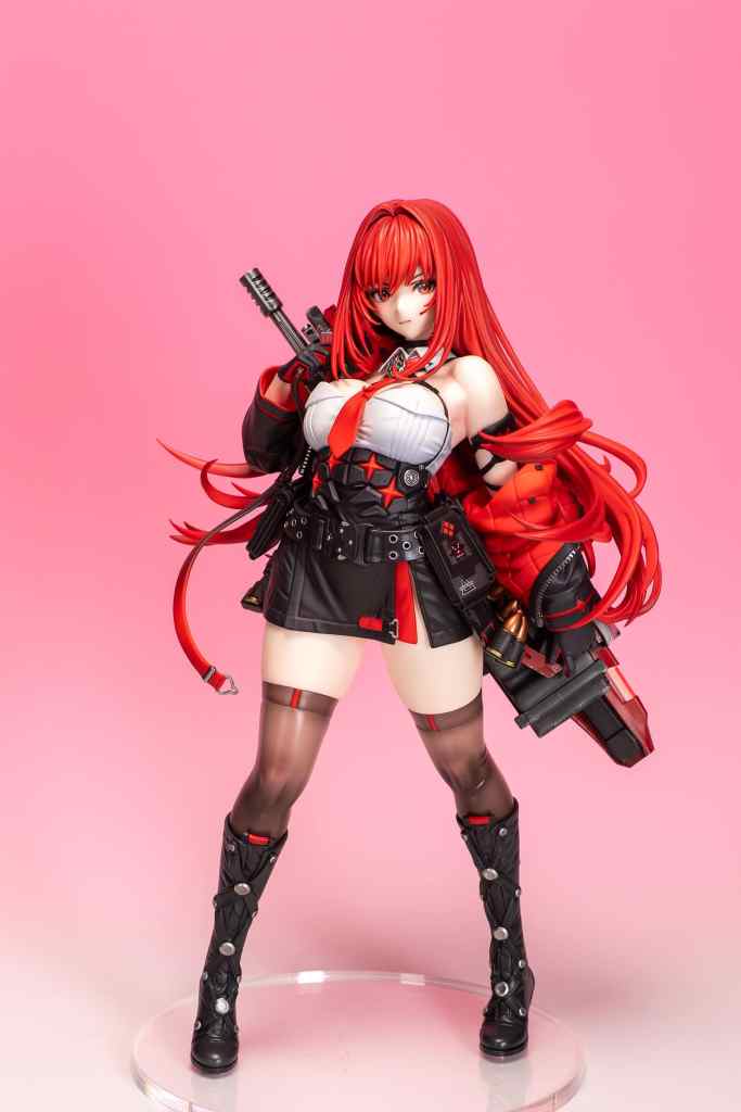 A detailed figure of a character with long red hair, dressed in a black and white outfit, holding a weapon and posing confidently. The background is a soft pink.