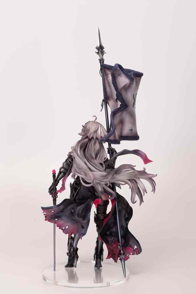 A detailed figurine of a character with long, flowing silver hair, wearing dark armor and a long cape. The character holds a staff topped with a pink orb and a flag with intricate designs, viewed from the back.