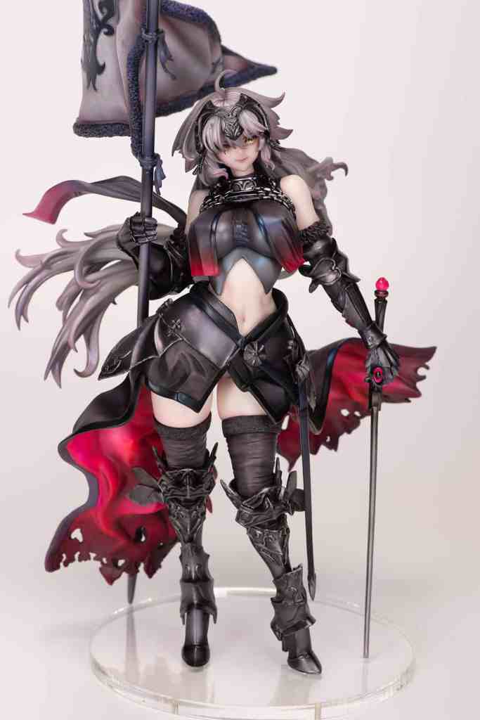 A detailed figurine of a character dressed in dark armor with a flowing red cape, holding a flag and a staff, featuring intricate design elements and a captivating pose.
