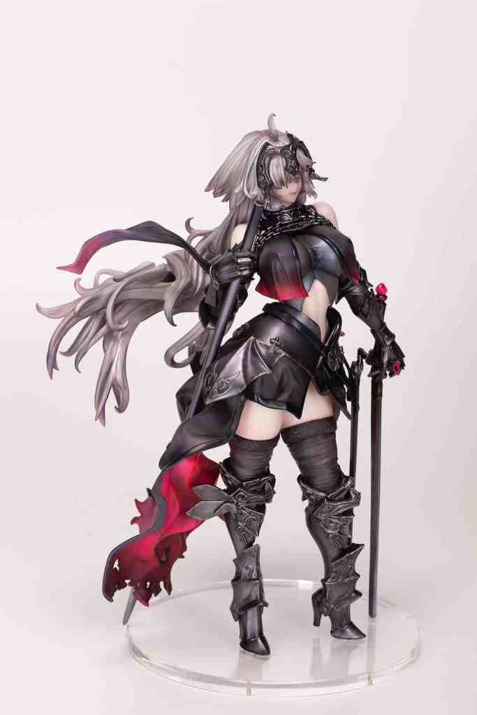 A detailed figurine of a female character in a dark, stylish outfit, featuring long flowing hair, a decorative headpiece, and holding a staff. The character has intricate clothing designs with a mix of black and red colors.