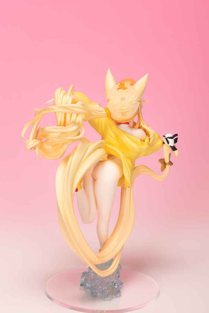 A figurine of a character with long flowing blonde hair, wearing a yellow outfit and a decorative mask. The character is posed dynamically on a clear base with a pink gradient background.